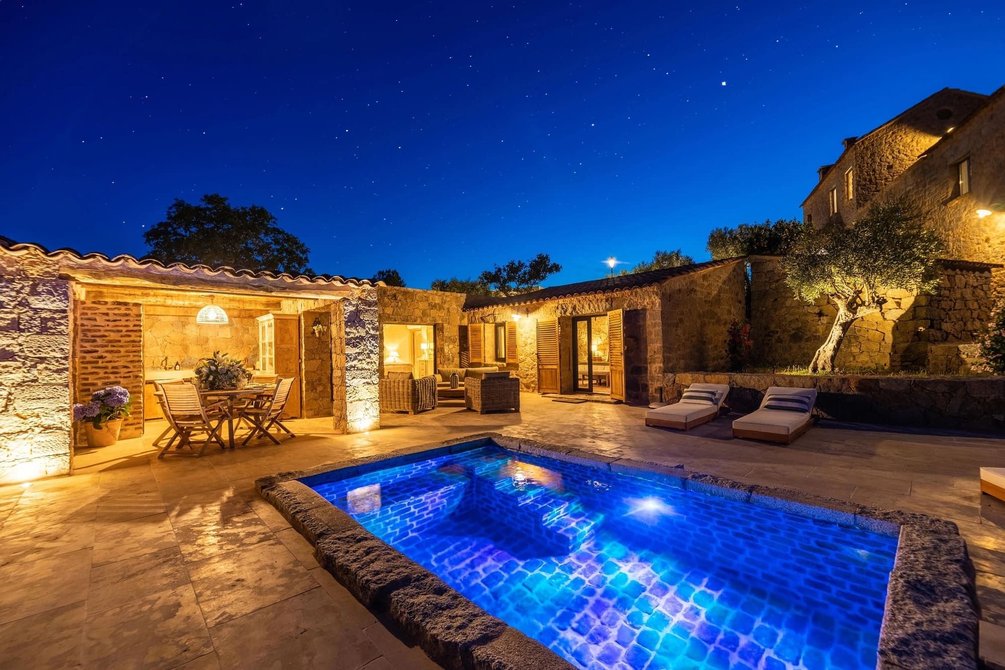 Domaine de charme avec piscine illuminée et terrasse en pierre sous le ciel étoilé