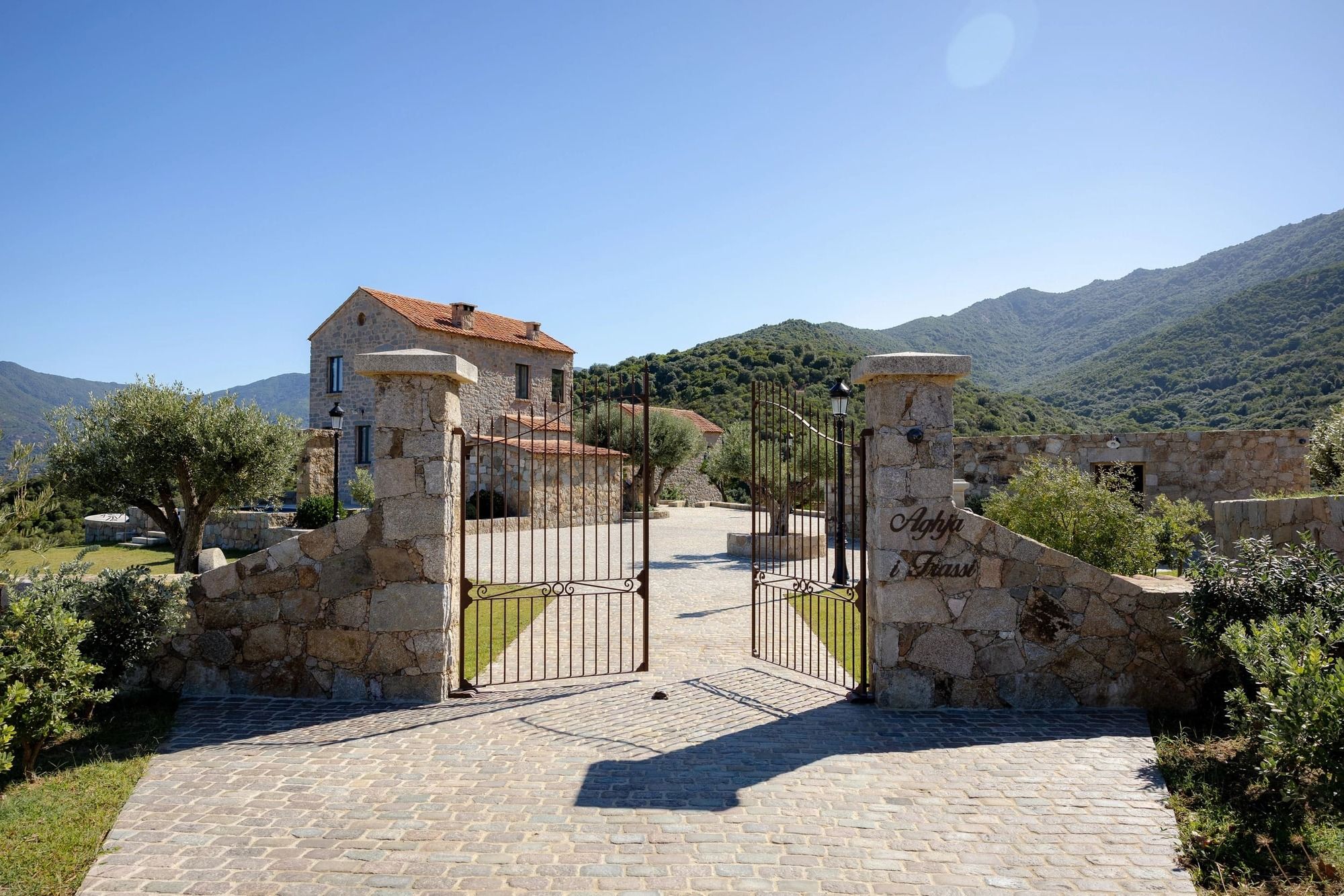 Domaine de charme avec portail en fer forgé, maison en pierre et montagnes boisées